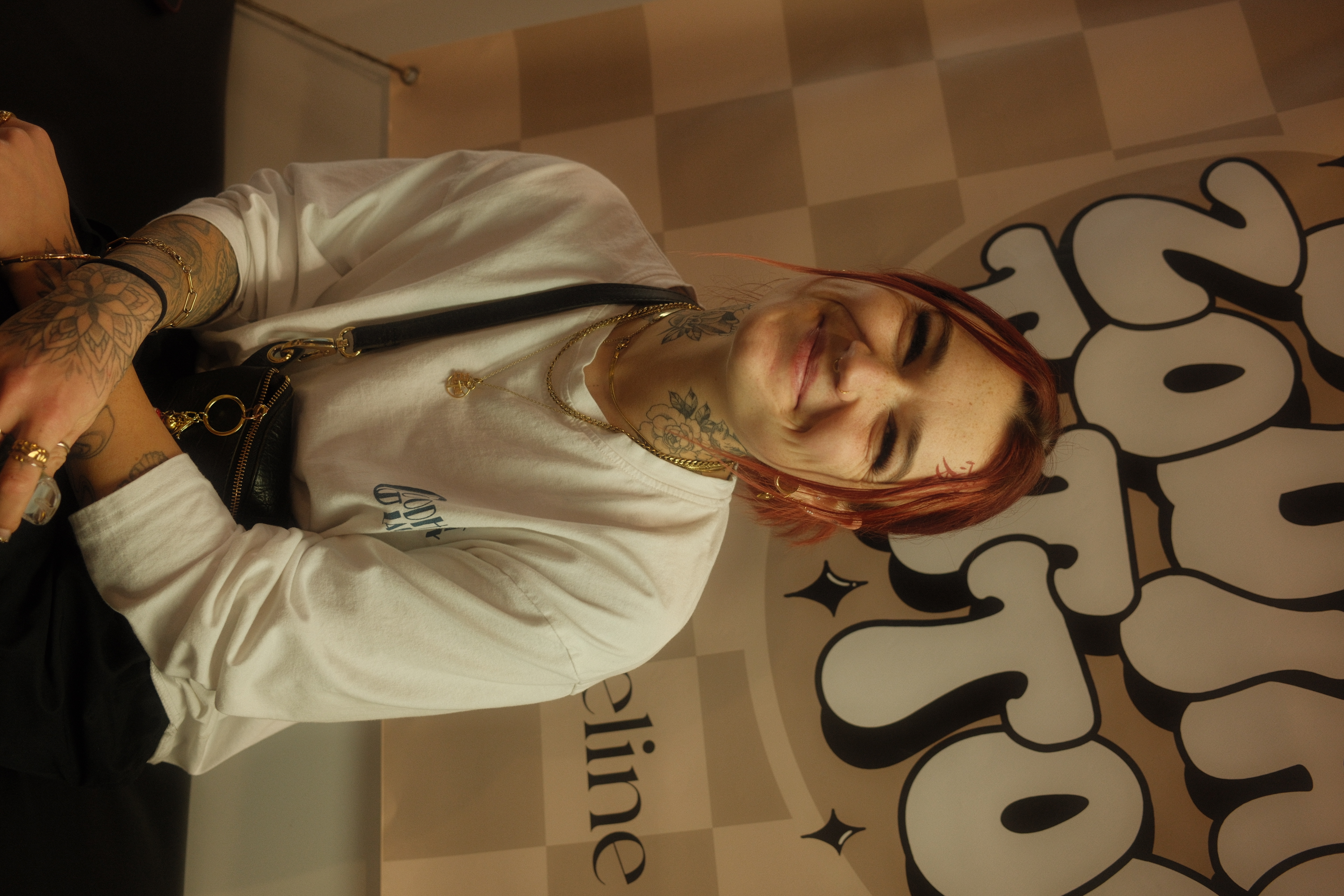 Ich sitze lächelnd im Studio vor einem Tattoo-Banner.